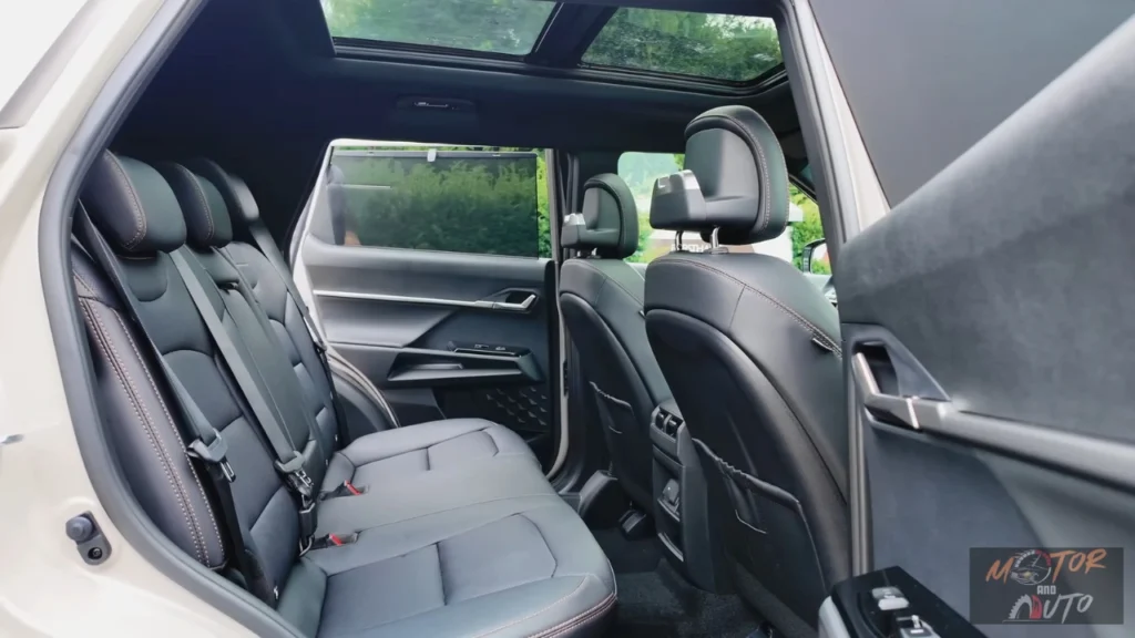 Interieurzicht vanuit achterdeur van 2025 KGM Torres Hybrid met ruime achterbank met grijze lederen stoelen, royale beenruimte, panoramisch schuifdak en zicht door naar voorstoelen met natuurlijke verlichting