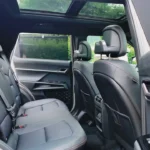 Interieurzicht vanuit achterdeur van 2025 KGM Torres Hybrid met ruime achterbank met grijze lederen stoelen, royale beenruimte, panoramisch schuifdak en zicht door naar voorstoelen met natuurlijke verlichting