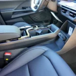 Close-up van 2025 KGM Torres Hybrid middenconsole met zwevend ontwerp met opbergruimte eronder, verchroomde bekerhouders, draadloze oplaadplaat, elektronische versnellingspook en grijze lederen stoelen met contrasterende stiksels