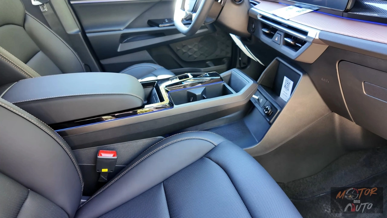 Close-up van 2025 KGM Torres Hybrid middenconsole met zwevend ontwerp met opbergruimte eronder, verchroomde bekerhouders, draadloze oplaadplaat, elektronische versnellingspook en grijze lederen stoelen met contrasterende stiksels