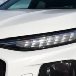 Gedetailleerd zicht van 2026 Audi Q3 slanke horizontale LED-lichtbalk met zichtbare micro-LED-segmenten die onderscheidend verlichtingspatroon creëren, geïntegreerd in koplamp assembly boven hoofdkoplamp unit op wit carrosseriepaneel