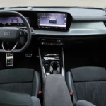Panoramisch breedhoekzicht van 2026 Audi Q3 interieur dashboard met gebogen dual-screen display, zwart sportstuurwiel met stuurpaddels, middenconsole opbergruimte en modern interieurontwerp met zacht-touch materialen