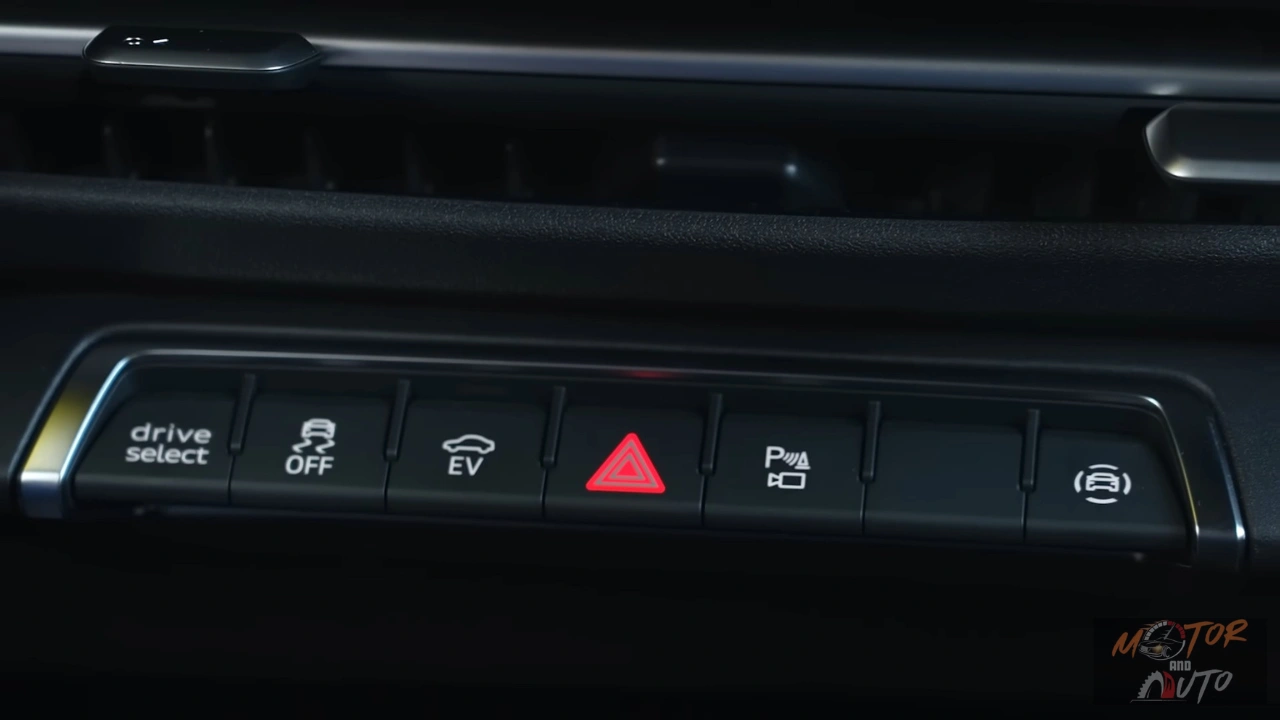 De middenconsole van de 2026 Audi Q3 met Drive Select knop, stabiliteitscontrole uitschakelaar, EV-modusselector, waarschuwingslichten voor gevaar, parkeerassistent knop en elektronische parkeerrem, allemaal gerangschikt in een strakke, minimalistische lay-out.