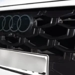 Gedetailleerde close-up van de kenmerkende Singleframe grille van de 2026 Audi Q3 met zwart honingraatpatroon, plat tweedimensionaal Audi vier ringen logo, radarsensoren geïntegreerd achter de grille en zwarte glanzende afwerking rondom op witte carrosserie.