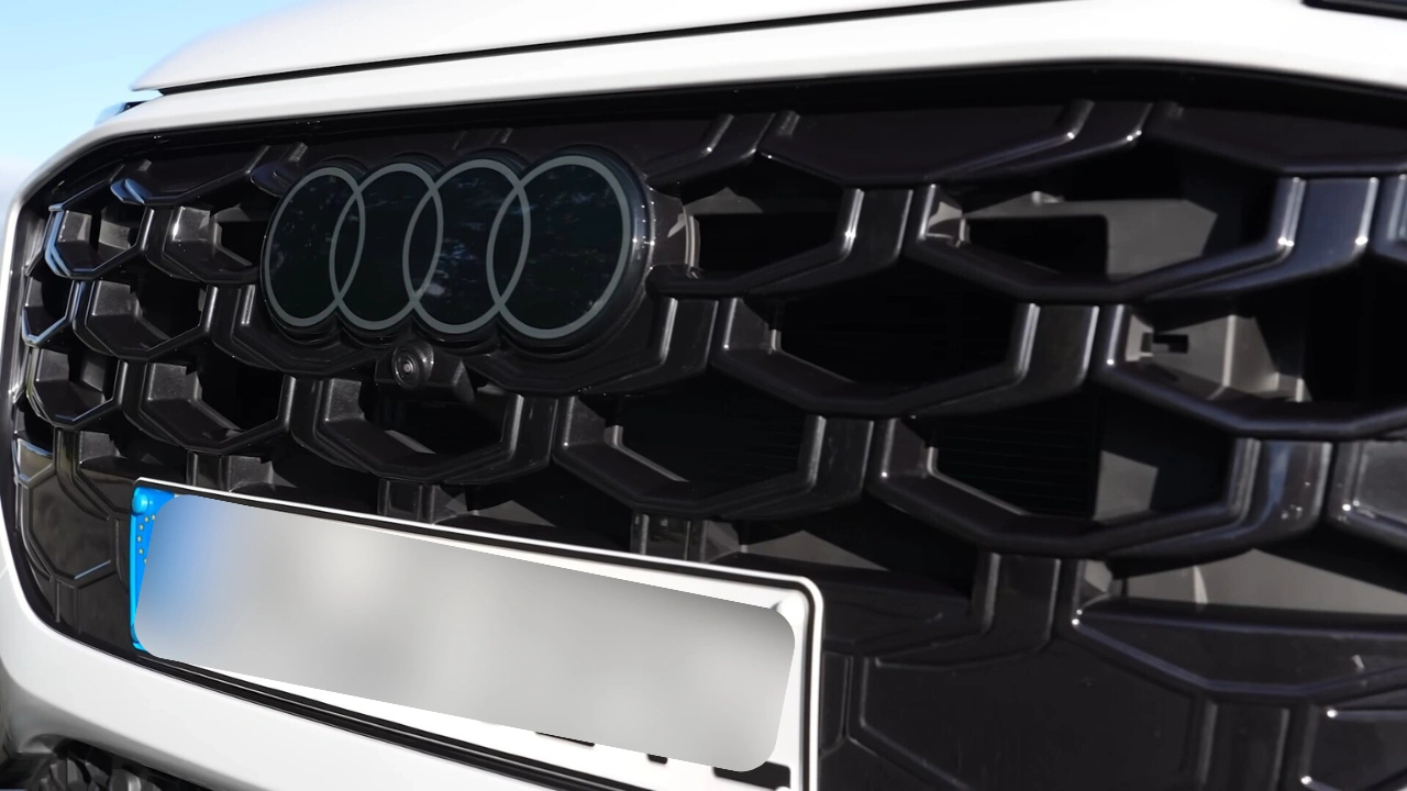 Gedetailleerde close-up van de kenmerkende Singleframe grille van de 2026 Audi Q3 met zwart honingraatpatroon, plat tweedimensionaal Audi vier ringen logo, radarsensoren geïntegreerd achter de grille en zwarte glanzende afwerking rondom op witte carrosserie.