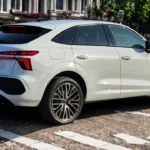 Gedetailleerd achter driekwart zicht van de 2026 Audi Q3 Sportback in stedelijke setting, met nadruk op de fastback daklijn integratie, gesplitste LED-achterlichten op twee niveaus, 20-inch veelspaaks wielen, zwarte onderste carrosseriebescherming en compacte 4.530mm totale lengte in premium witte afwerking.