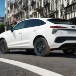 De 2026 Audi Q3 Sportback in Gletsjerwit met zijn aflopende daklijn, gesplitste LED-achterlichten met horizontale lichtstrook, 20-inch veelspaaks zwarte wielen met rode remklauwen en compacte SUV-proporties in een stedelijke Europese setting.