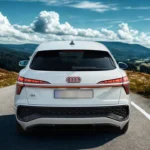 Rear view of the 2026 Audi Q3 Sportback on mountain road showcasing split-level LED taillights with horizontal connecting light strip, illuminated Audi rings (market-dependent), roof-mounted shark fin antenna, rear wiper, black lower diffuser, and scenic highland backdrop.