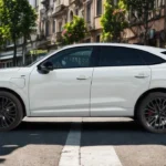 Compleet zijprofiel van de 2026 Audi Q3 Sportback met zijn 4.530mm lengte, fastback daklijn, prominente schouderlijn, zwarte spiegelkappen, vlakke deurgrepen, 20-inch wielen, plug-in hybride oplaadpoort op voorspatbord en zwarte onderste carrosseriebescherming in stedelijke setting.