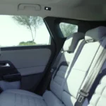 Achtercabine weergave van 2026 Citroën C5 Aircross met lichtgrijze bankzit, panoramisch glazen schuifdak, ruim interieur, en zijraam vanuit binnenkant voertuig