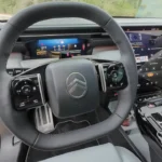 2026 Citroën C5 Aircross met leer bekleed stuurwiel met chromen accenten, knopbediening aan beide zijden, Citroën logo in het midden, en digitaal instrumentenpaneel zichtbaar erachter met navigatie display