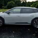 De 2026 Kia EV4 fastback toont zijn gestroomlijnde aerodynamische profiel en 19-inch wielen op nat wegdek met natuurlijke omgeving