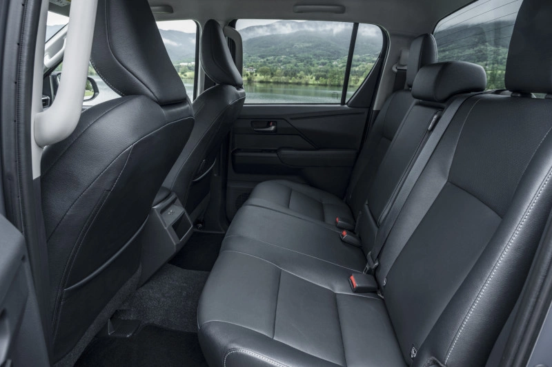 Achterbank van de 2026 Toyota Hilux BEV Double Cab in zwart leder met uitzicht op een meer.