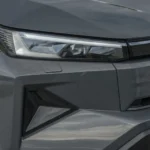 Close-up van de slanke LED-koplamp en grille-loze voorzijde met geometrische textuur van de 2026 Toyota Hilux BEV in Ash Grey.