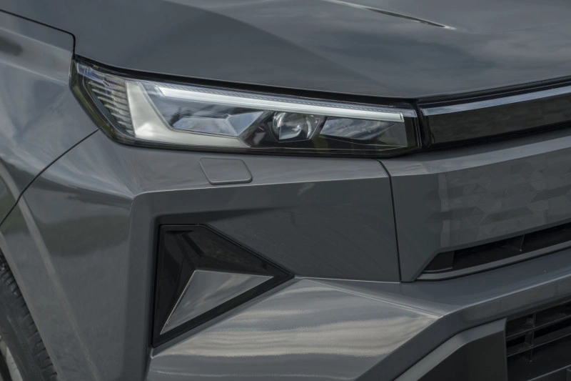 Close-up van de slanke LED-koplamp en grille-loze voorzijde met geometrische textuur van de 2026 Toyota Hilux BEV in Ash Grey.