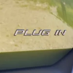 Close-up van het chromen 'Plug In'-embleem op de groene 2026 Peugeot 408.