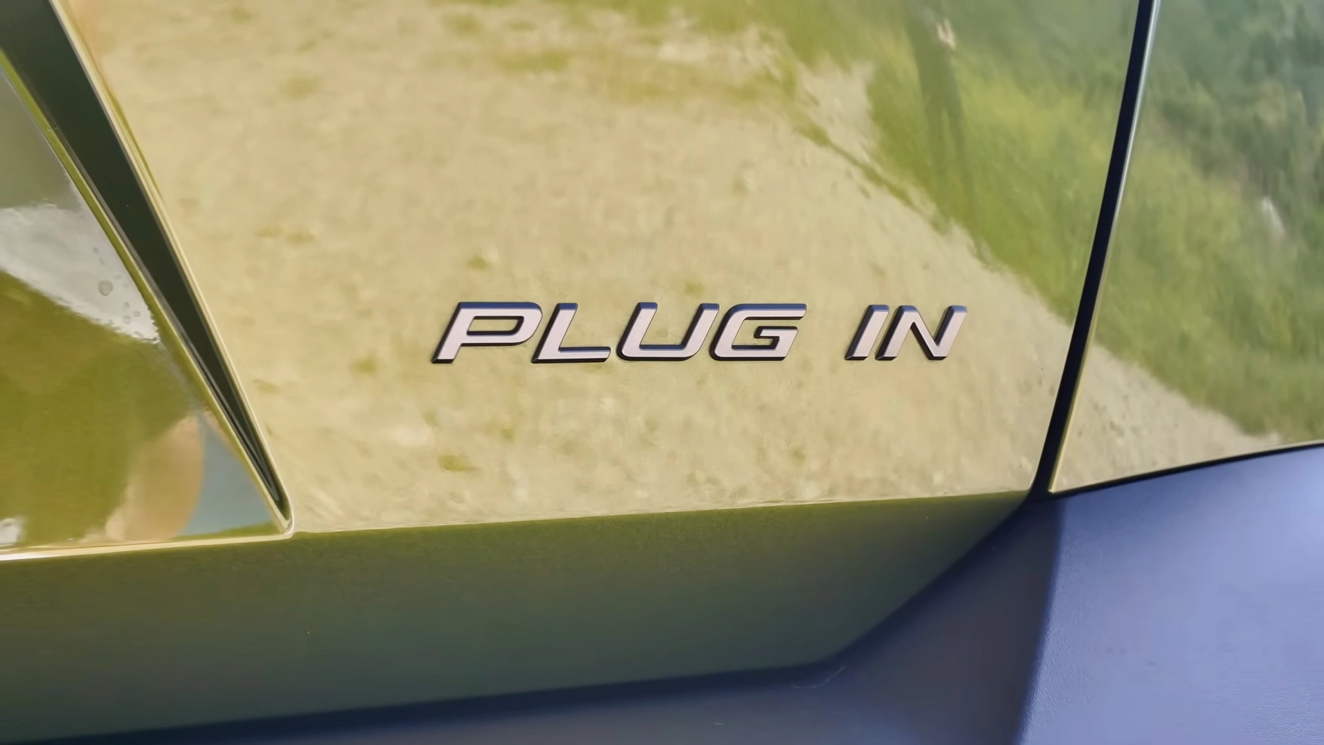 Close-up van het chromen 'Plug In'-embleem op de groene 2026 Peugeot 408.