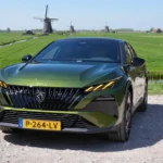 Recht vooraanzicht van de groene 2026 Peugeot 408 met molens op de achtergrond.