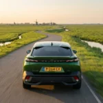Achteraanzicht van een groene 2026 Peugeot 408 op een kronkelweg door weiland.
