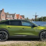 Zijaanzicht van de groene 2026 Peugeot 408 bij een kanaal met Hollandse huizen.