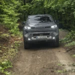 2026 Toyota Hilux BEV op een modderig bospad, vooraanzicht met brandende koplampen, die de off-road kwaliteiten toont.