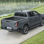 Achteraanzicht driekwart van de 2026 Toyota Hilux BEV in Ash Grey aan een meer, met zicht op de open laadbak.