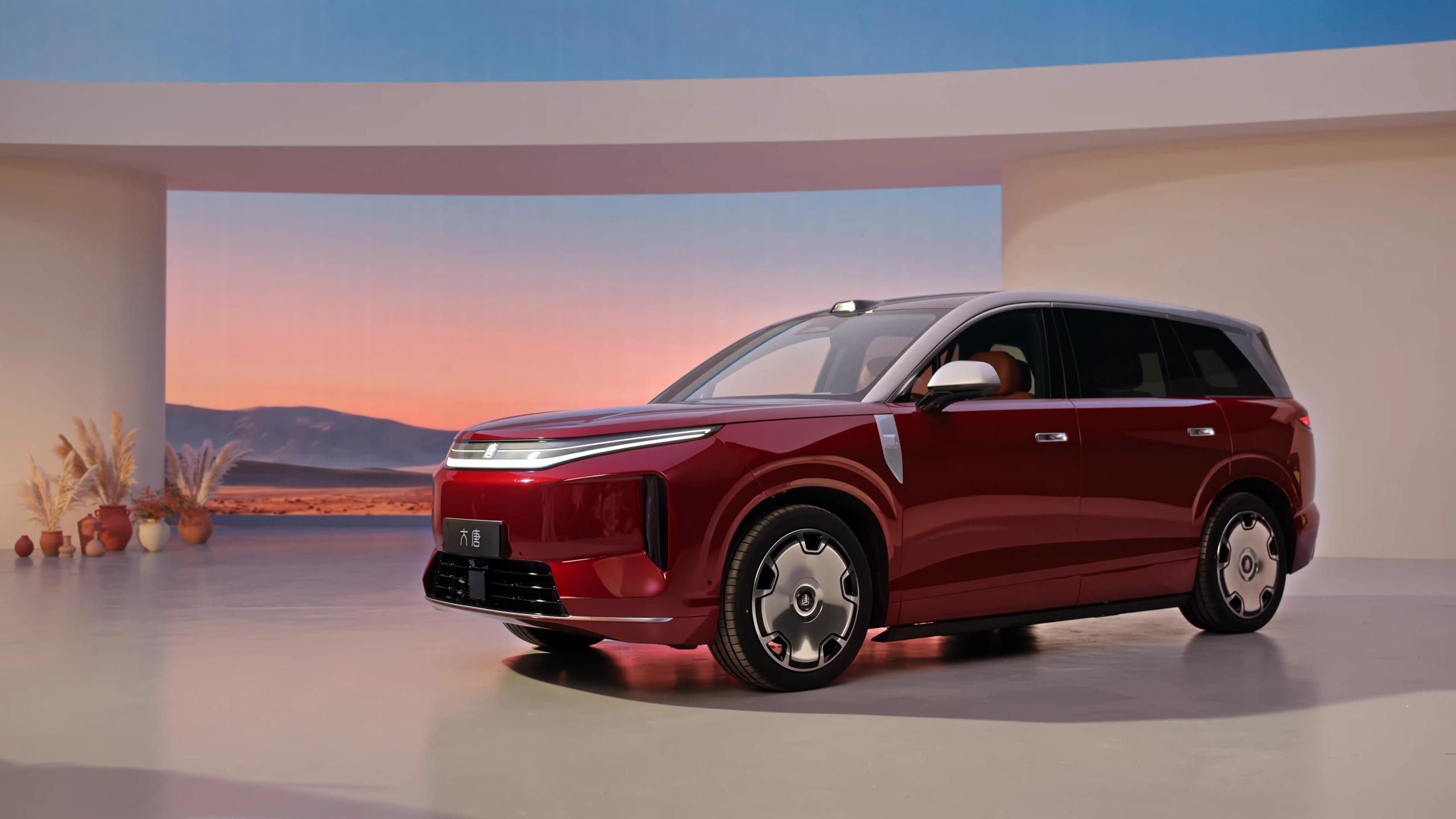 Rode BYD Great Tang volwaardige elektrische SUV in een studio met een woestijnzonsondergang en gedroogd pampasgras.