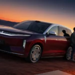 Rode BYD Great Tang volwaardige elektrische SUV geparkeerd op een heuvel bij zonsondergang met een man ernaast.