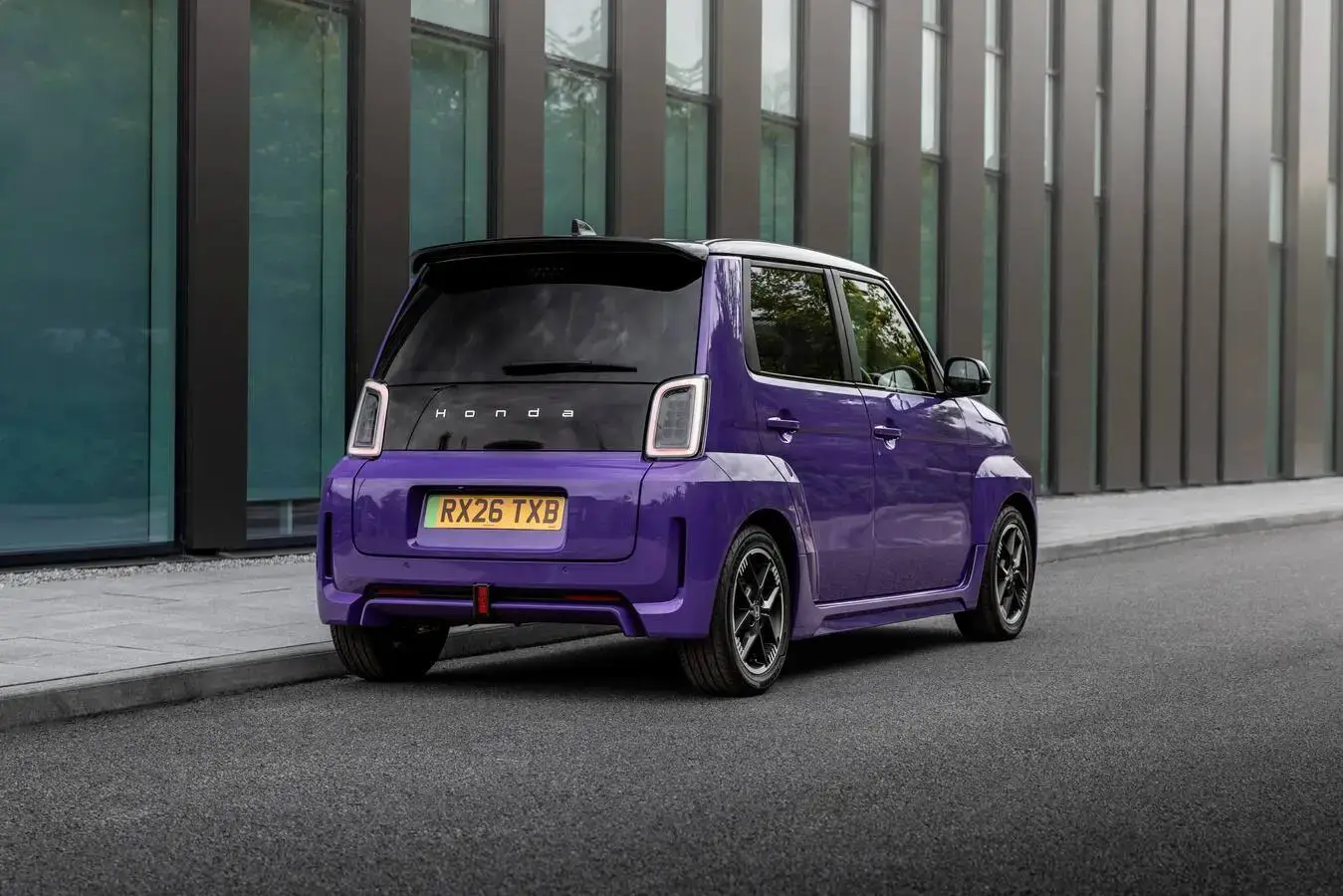 Achteraanzicht schuin van een paarse Honda Super-N elektrische stadsauto langs de stoeprand.