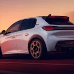 Witte Peugeot e-208 GTi in beweging, achterkwartaanzicht met de uitgeklopte wielkasten, achterspoiler, diffuser en geperforeerde 18-inch velgen.