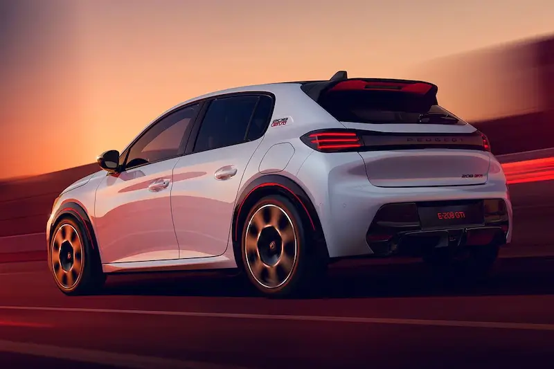 Witte Peugeot e-208 GTi in beweging, achterkwartaanzicht met de uitgeklopte wielkasten, achterspoiler, diffuser en geperforeerde 18-inch velgen.