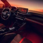 Dashboard en middenconsole van de Peugeot e-208 GTi met rode sfeerverlichting, touchscreen en tweekleurige sportstoelen.