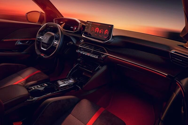 Dashboard en middenconsole van de Peugeot e-208 GTi met rode sfeerverlichting, touchscreen en tweekleurige sportstoelen.