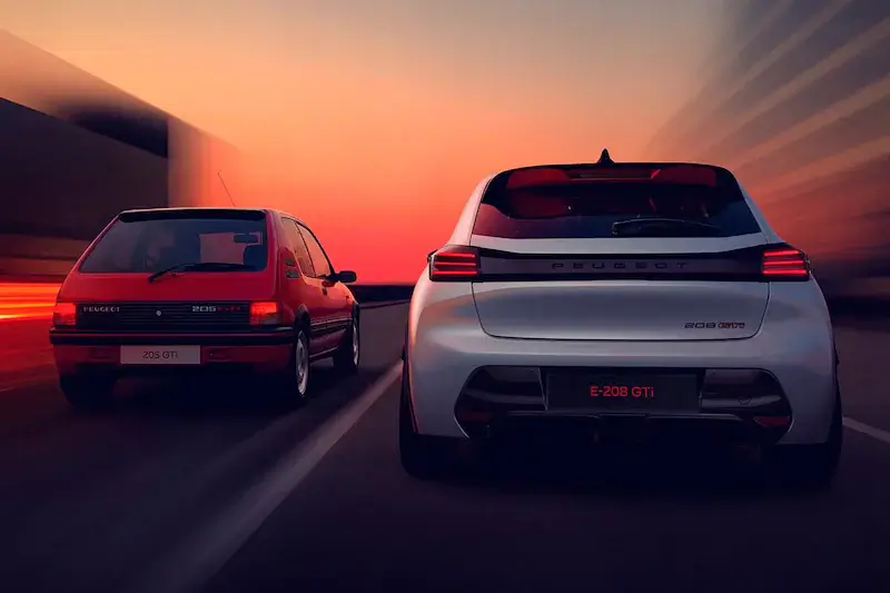 Achteraanzicht van de witte Peugeot e-208 GTi die naast de klassieke rode Peugeot 205 GTi rijdt bij zonsondergang.