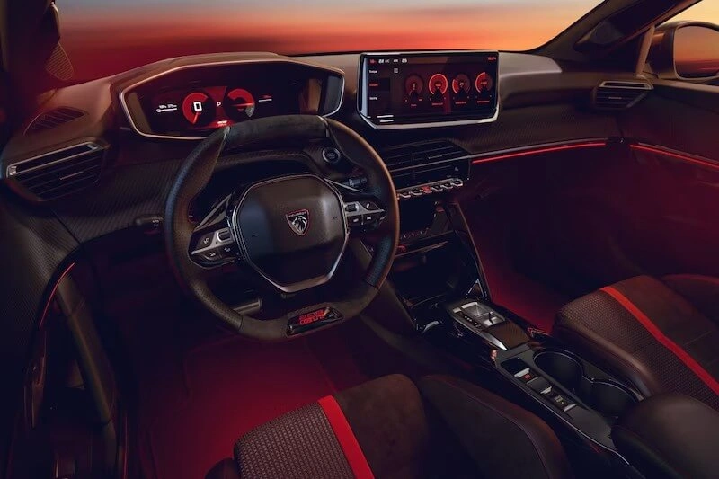 Interieur van de Peugeot e-208 GTi met het compacte GTI-stuurwiel, rood digitaal instrumentenpaneel en centraal touchscreen.