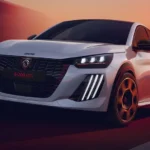 Witte Peugeot e-208 GTi in beweging, vooraanzicht met de grille met rode accenten, drieklauws-LED-koplampen en 18-inch velgen.