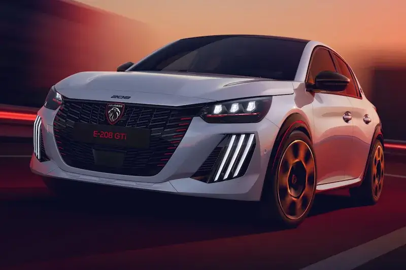 Witte Peugeot e-208 GTi in beweging, vooraanzicht met de grille met rode accenten, drieklauws-LED-koplampen en 18-inch velgen.