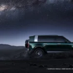 Zijaanzicht van de groene Stelato G9 off-road SUV met een reservewiel achterop, geparkeerd in een woestijn onder de Melkweg.